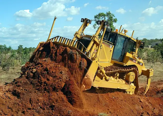 Bulldozer pushing a pile of red earth on a cleared site