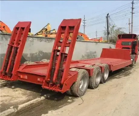 Red lowbed trailer with its loading ramps raised, hitched to a truck