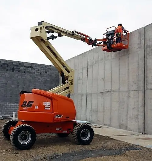 Boom lift with a worker in the raised platform beside a concrete wall